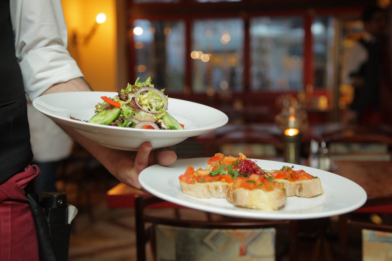 A waiter serves a fresh salad and hors doeuvres in a cozy restaurant setting.